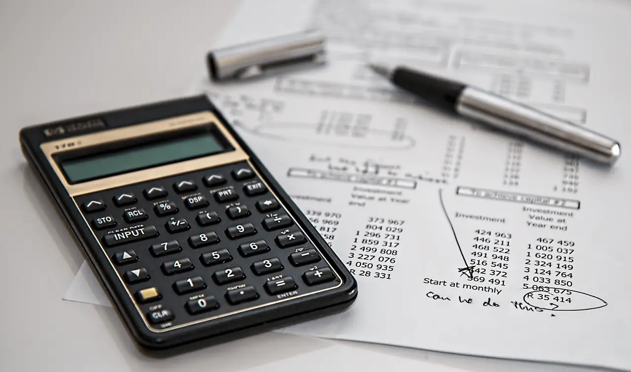The image shows a calculator a paper and a pencil on a table.