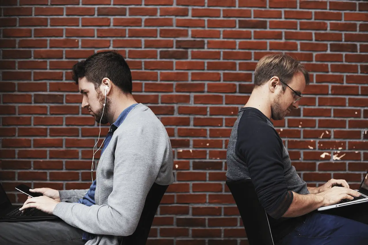 The image shows two men seating  and using mobile devices.