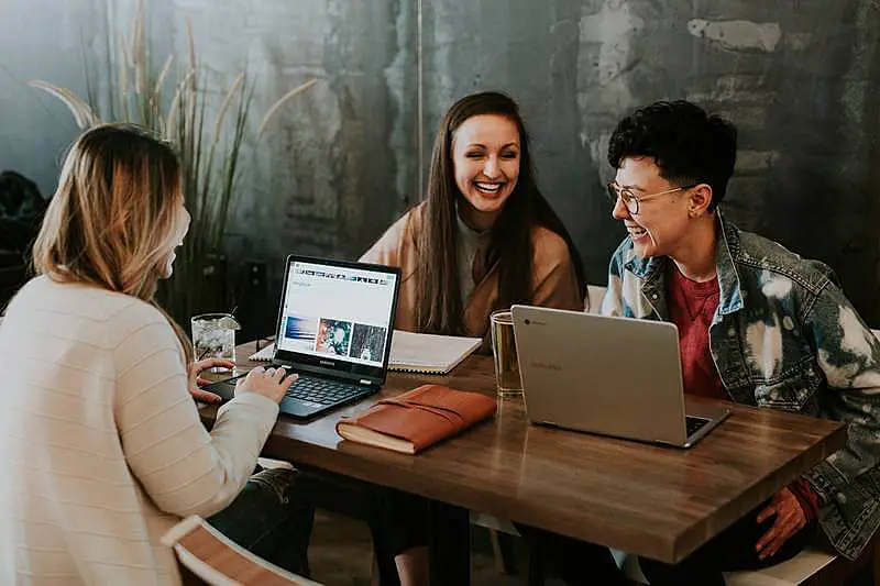 The image shows three people sitting around a table working together, and laughing,