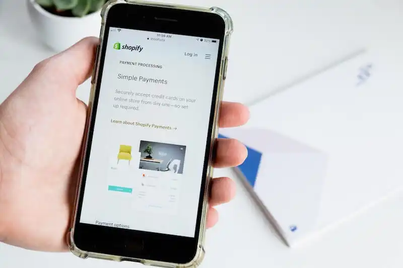 The image shows someone holding a smartphone, on its screen there is Shopify Payments page.