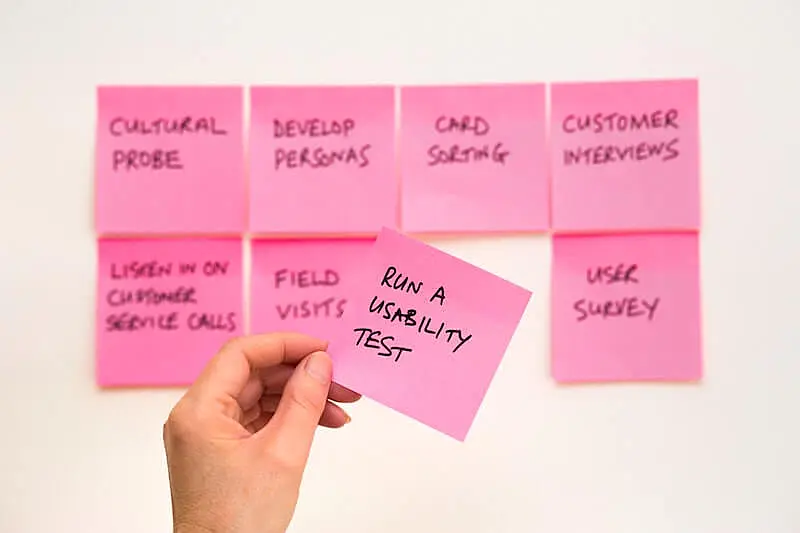 The image shows several post-its on a wall, a hand holds one pos-it where it's written "Run a usability test".