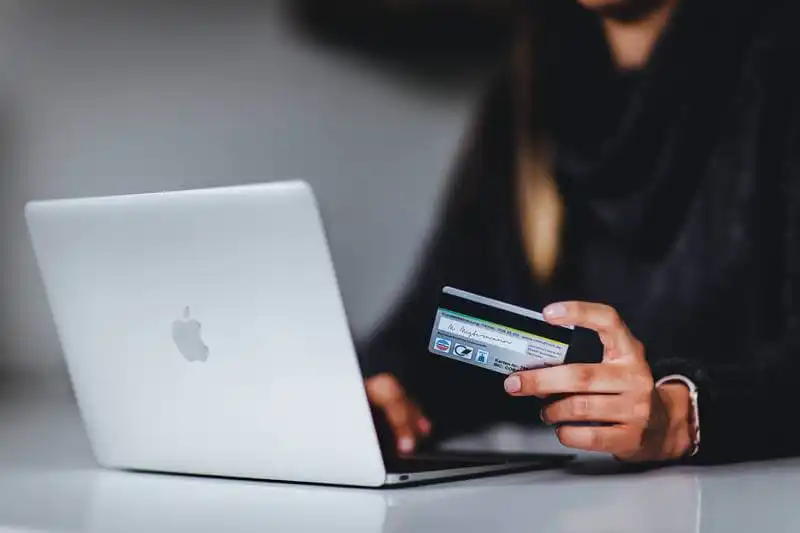 The image shows a woman holidn a credit cart in front of a laptop