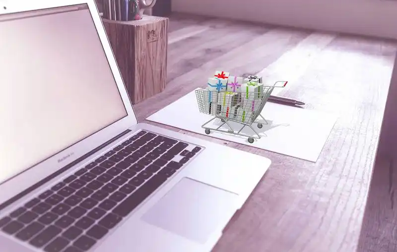 The image shows a laptop on a table, and on its right side there is a mini shopping cart full of wrapped gifts