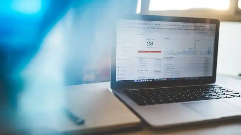 The image shows a laptop on a table, in the screen of the laptop there are some metrics being shown.