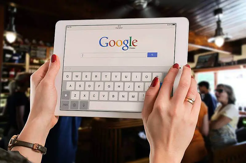 The image shows a woman holding a tablet, on the screeen there is Google's home page.