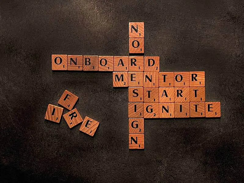 The image shows a word board game. The words "onboard, mentor, start, ignite, no resign, and fire" are written.