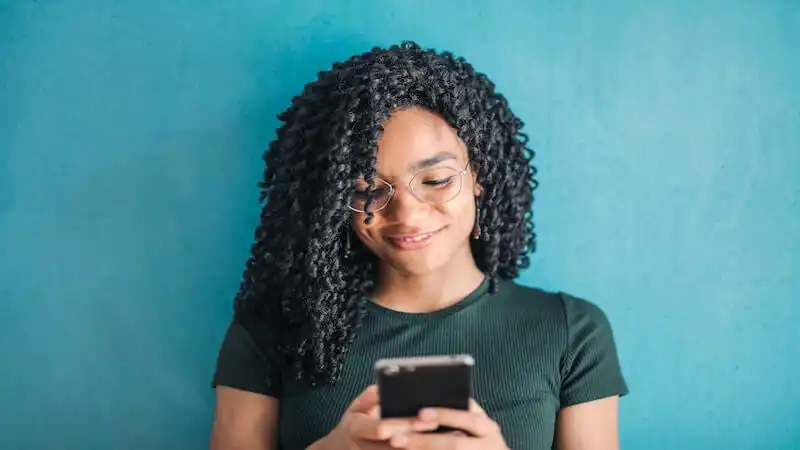 The image shows a woman using a smartphone, and smiling.