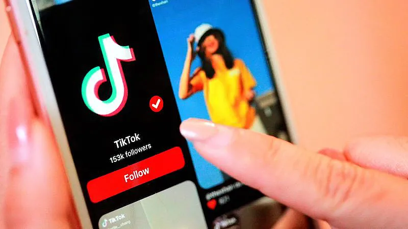 The image shows a person holding a smartphone, in the smartphone screen there is an image from the TikTok app.