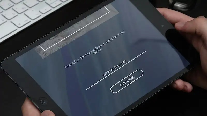 The image shows a person holding a tablet, on the screen, it's written "Please, fill in the required fields to subscribe to our service. "