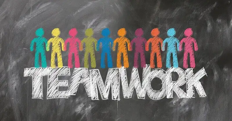 The image shows a chalk board whrere there is a drwaing of multiple people side by side and underneath, it's written teamwork.