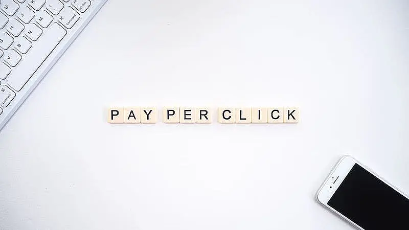  The expression "pay per click"  is written in the middle of the image, on the upper left side there is a keyboard, and on the inferior right side there is a smartphone.