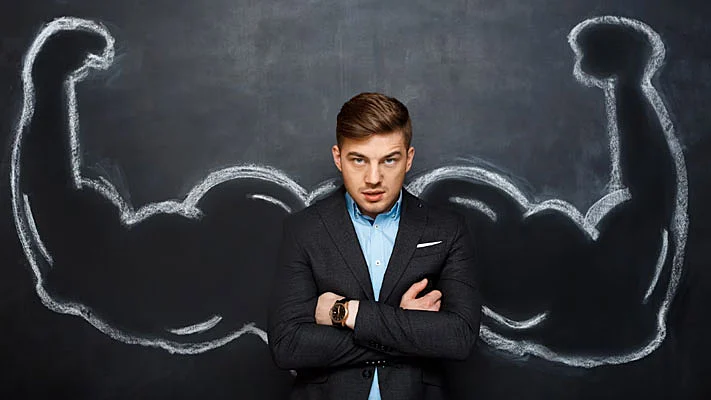 Foto de un hombre frente a una pizarra, en que están dibujados brazos fuertes