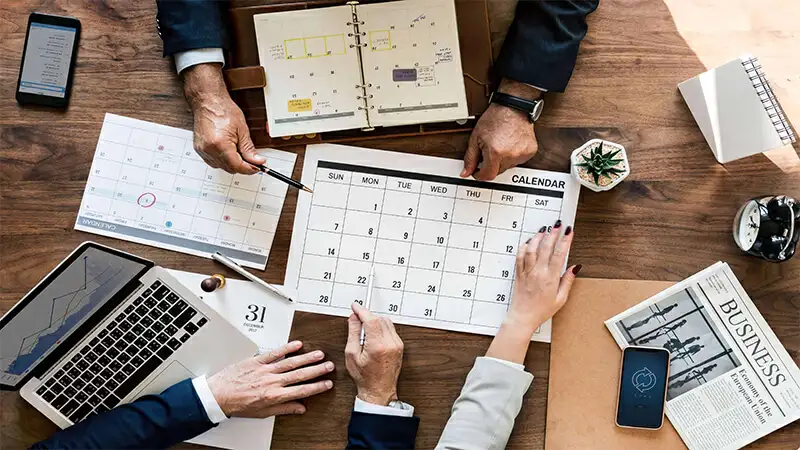 Calendário Comercial Foto de pessoas sentadas em uma mesa ao redor de um calendário