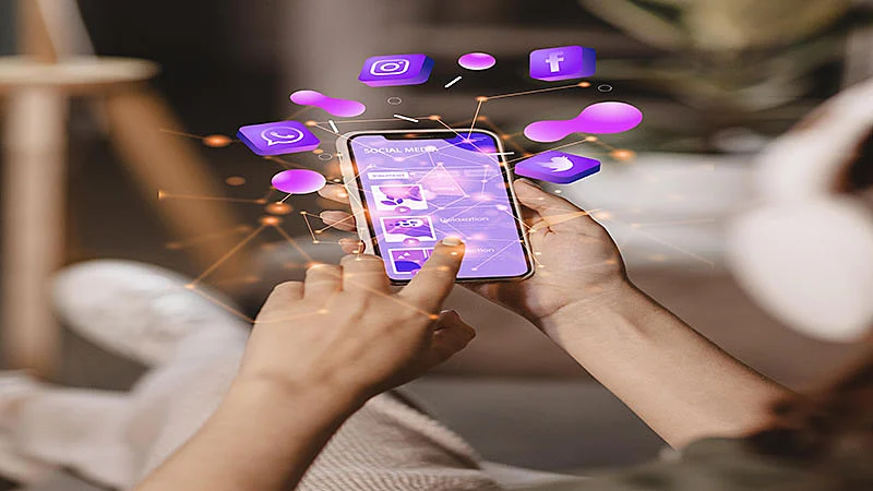 Foto de uma pessoa usando o celular e icones das redes sociais na tela