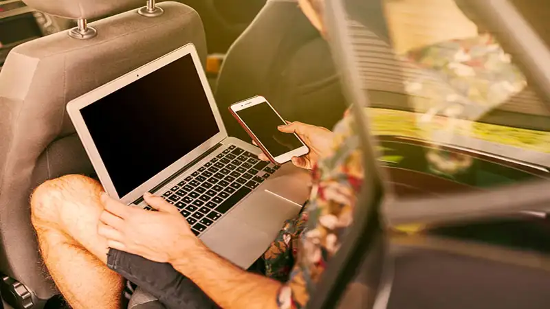 Foto de uma pessoa usando um notebook e um celular dentro de um carro