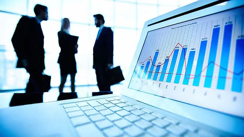Foto de gráficos no primeiro plano e duas pessoas dando as mãos ao fundo