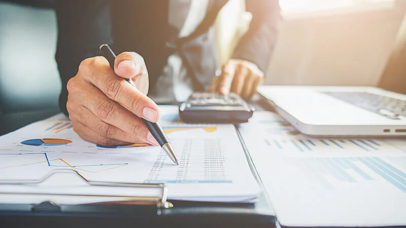 Foto de uma pessoa utilizando um notebook, calculadora e analisando planilhas