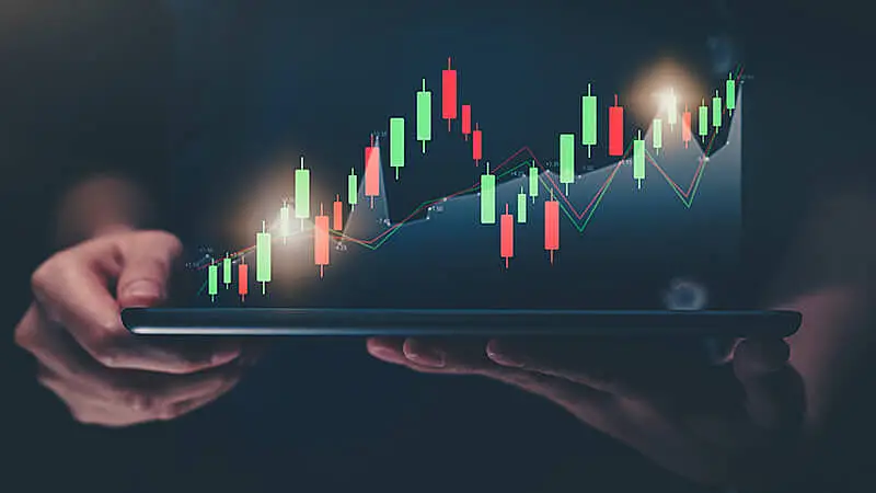 Foto de uma pessoa usando um notebook com gráficos subindo e descendo na tela.