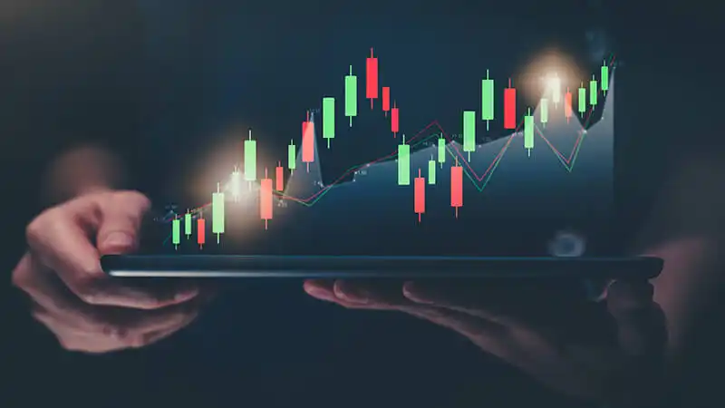Como investir na bolsa de valores Foto de uma pessoa usando um notebook com gráficos subindo e descendo na tela.