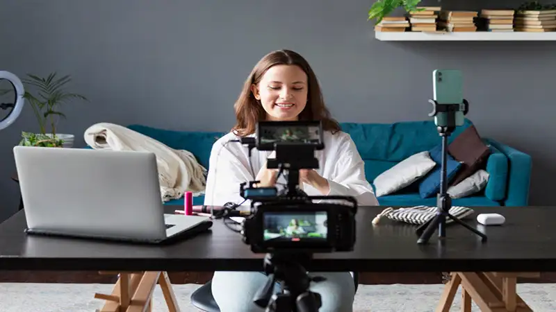 como monetizar o youtube Foto de uma mulher gravando um vídeo com algumas cameras e um notebook em cima de uma mesa