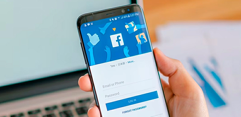 Pessoa mexendo no celular enquanto está com Facebook aberto no notebook