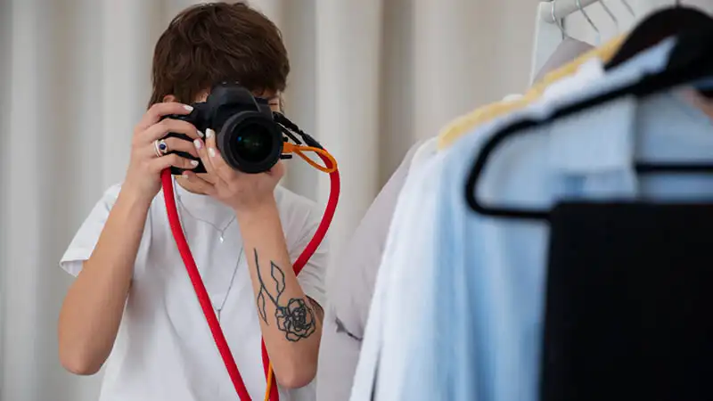 como tirar fotos de roupas para vender Foto de uma mulher tirando fotos de roupas penduradas em cabides