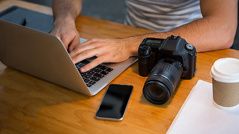 Foto de uma pessoa mexendo em um notebook em cima da mesa com câmeras