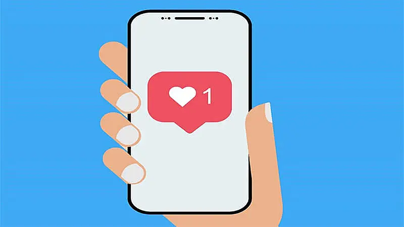 Imagem de uma mão segurando um celular com um ícone de curtida do Instagram
