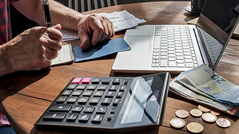 Foto de uma pessoa usando uma calculadora e analisando documentos