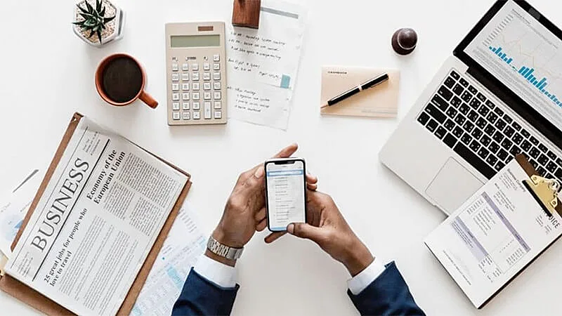 Pessoa apoiada em uma mesa com celular na mão e diversos gráficos e papeis em cima da mesa
