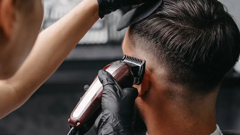 Foto de uma pessoa cortando o cabelo de um homem com maquina