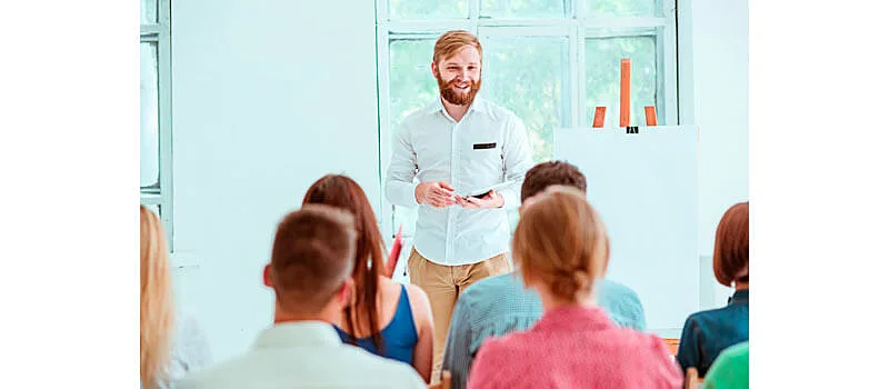 Homem segurando um tablet e fazendo uma apresentação para várias pessoas em uma sala