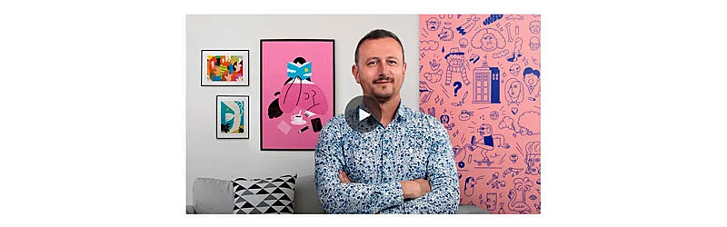 Professor Puño em primeiro plano e em segundo plano quadros com suas ilustrações pendurados na parede