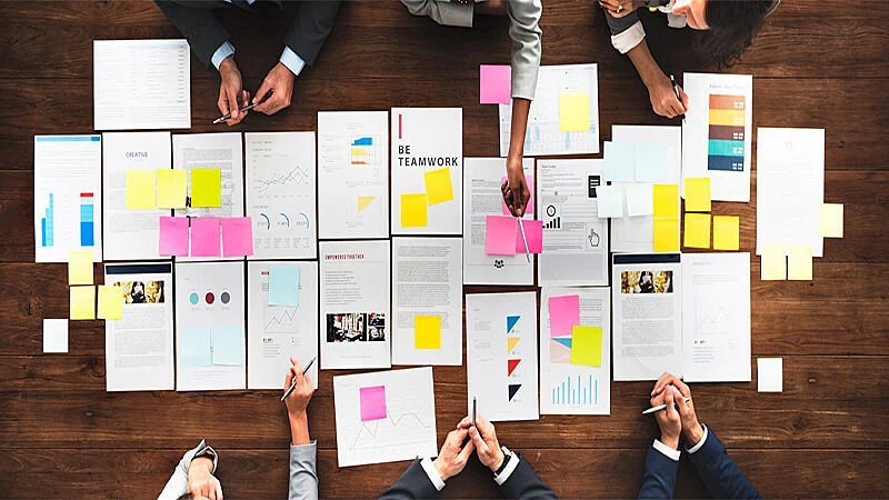 Foto de uma mesa de reunião com várias pessoas e papeis