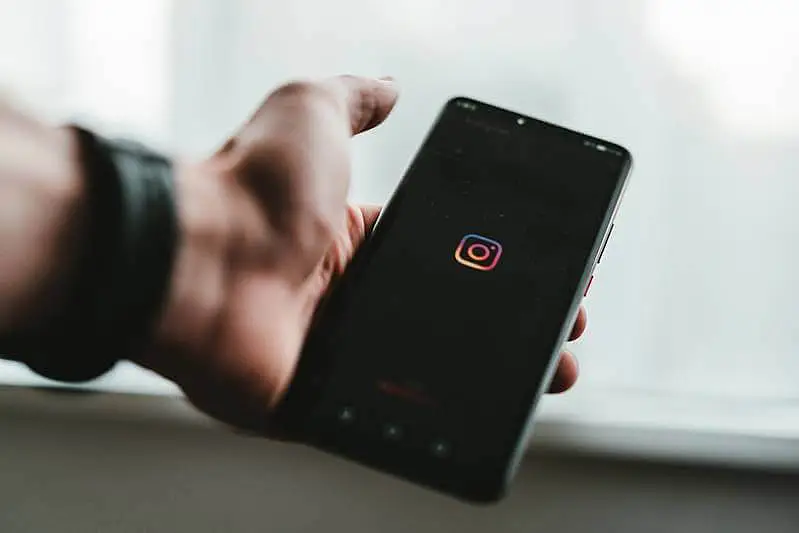 The image shows a person holdin a smarphone where it appears the Instagram icon.