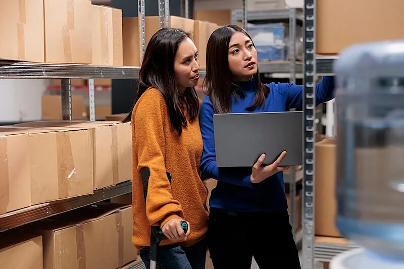 The image shows two women inside a warehouse