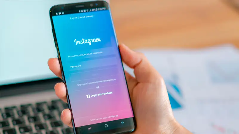 Foto de uma pessoa segurando um celular com a tela de login do Instagram