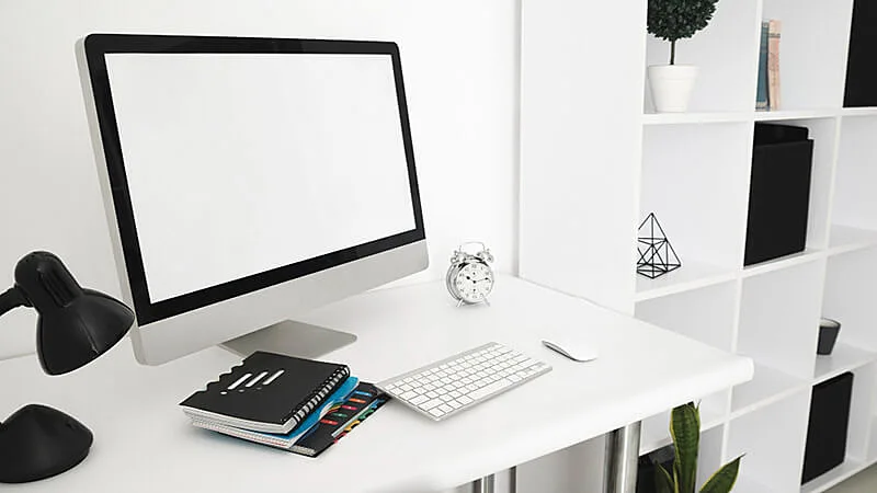 imagem que mostra uma tela de computador com um relógio marcando 13h09 em cima de uma mesa ao lado de um estante