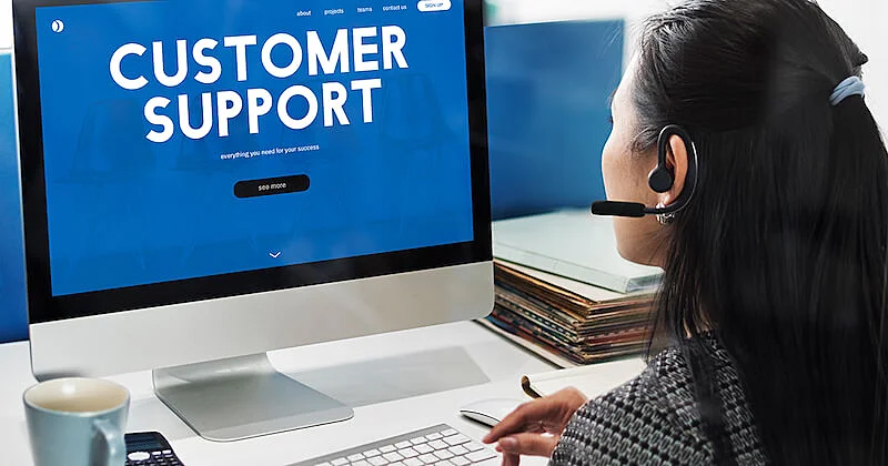 A woman in siiting in fron of a desktop computer. On the computer screen it's written "customer support".