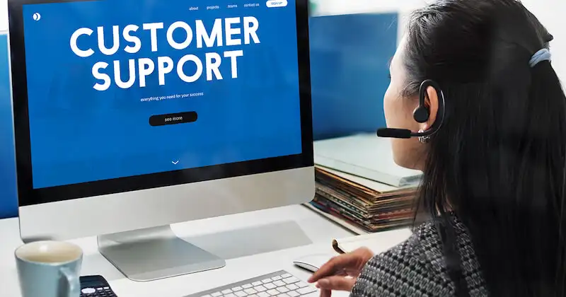 A woman in siiting in fron of a desktop computer. On the computer screen it's written "customer support".