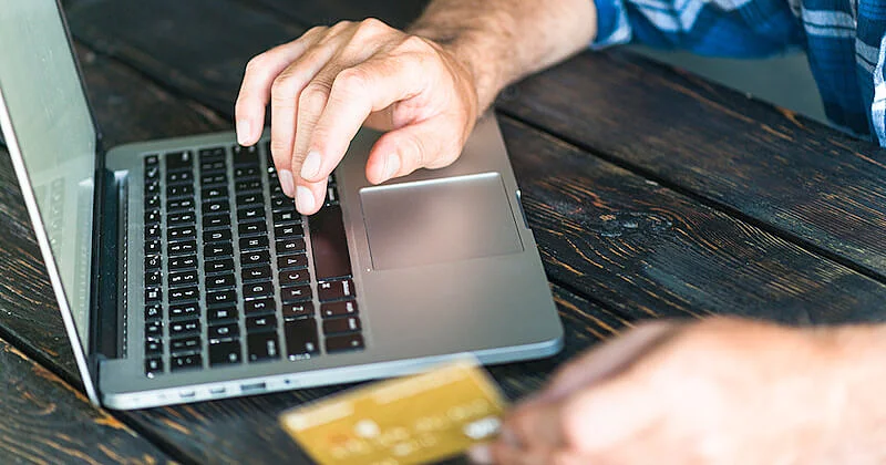 The image shows a man typing on a laptop keyboards, and holding a credit card.