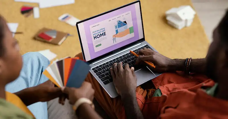 A person is in front of a laptop and the other one on their left side is holding a palette of colors. 
