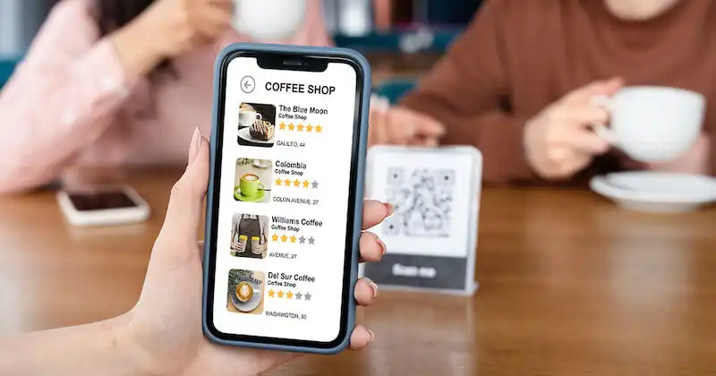 A woman is holding a smartphone. On its screen there is a list of coffee shops.