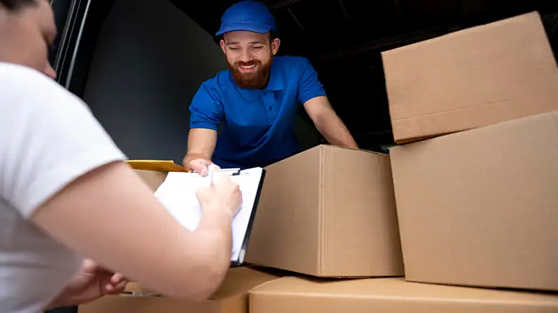 Foto de uma pessoa assinando um papel e um entregador com várias caixas