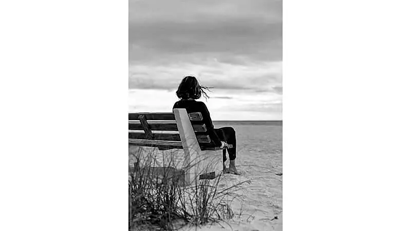 foto em preto e branco de uma mulher sentada em um banco na praia em um dia nublado