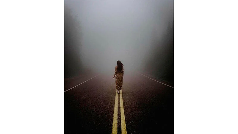 foto de uma mulher andando no meio de uma estrada com neblina