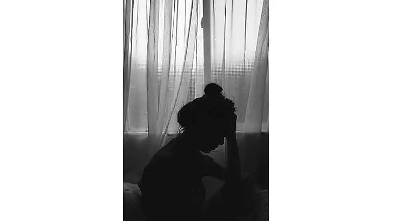 foto em preto e branco da silhueta de uma mulher triste com a mão no rosto