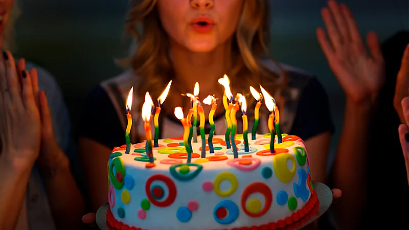 Foto de uma mulher assoprando velas em um bolo