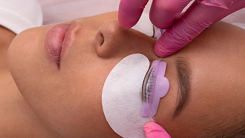 Foto de uma profissional fazendo o alongamento de cílios em outra mulher