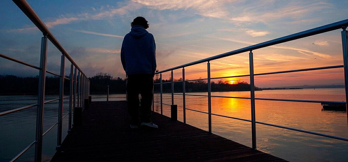 Foto de uma pessoa sentada em uma cerca olhando para o horizonte